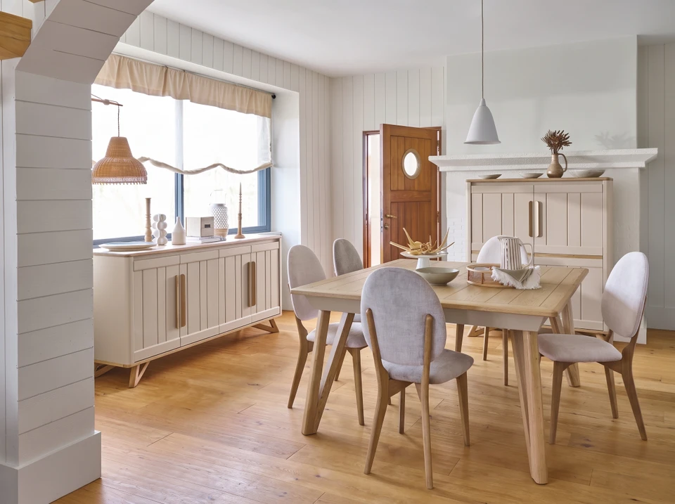 Personne tenant une tablette tactile affichant un canapé gris avec coussins orange en réalité augmentée dans un intérieur domestique minimaliste aux murs blancs et parquet bois clair